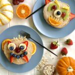 Overhead view of two blue plates with pancakes on the top. The pancakes are decorated with fruits and nuts to look like monsters.