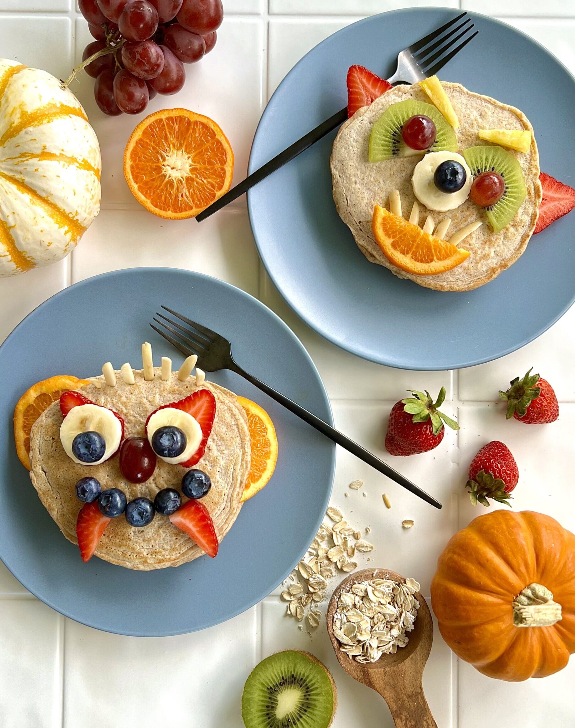 Overhead view of two blue plates with pancakes on the top. The pancakes are decorated with fruits and nuts to look like monsters.