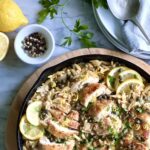 Overhead view of chicken, orzo, lemons in a beautiful brown dish with capers and lemons around the side.