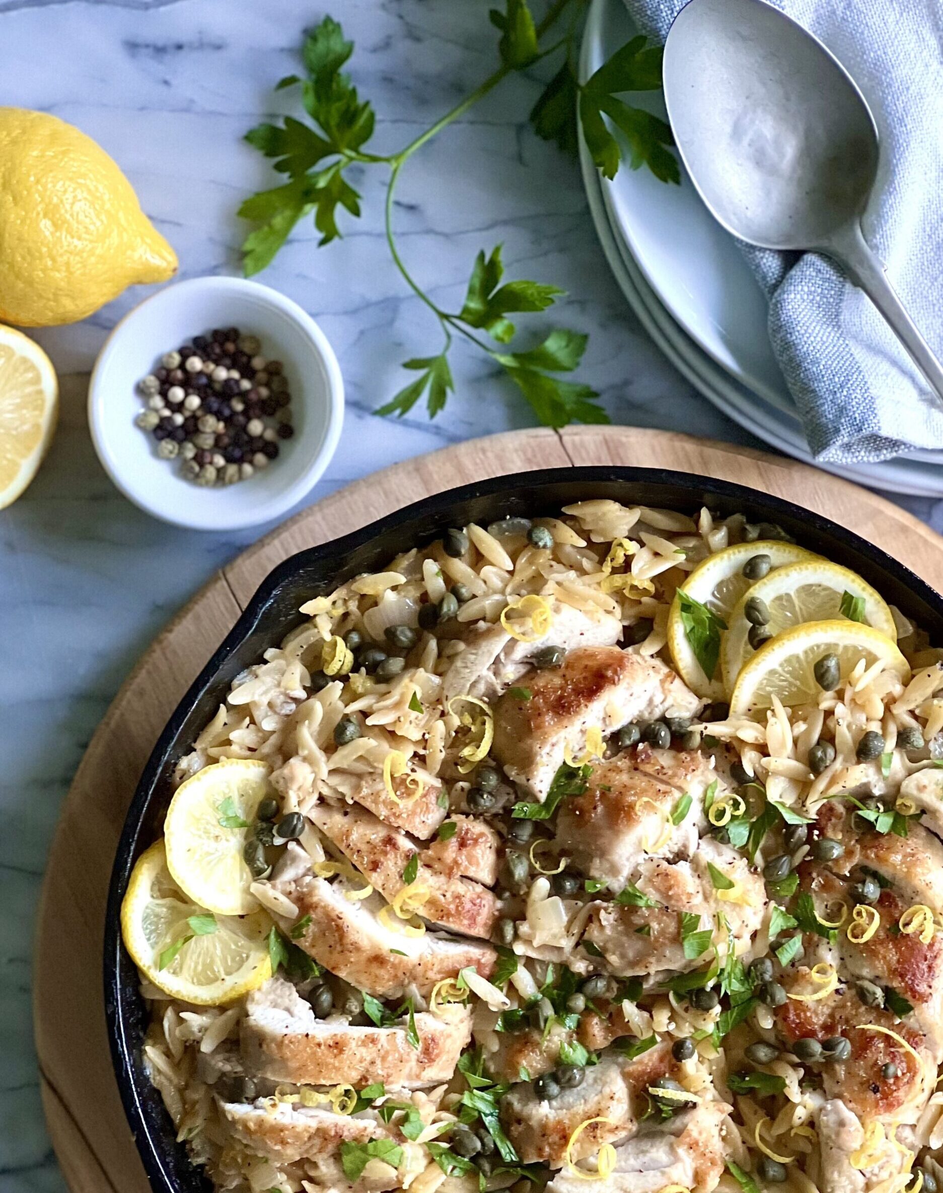 Overhead view of chicken, orzo, lemons in a beautiful brown dish with capers and lemons around the side.