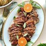 Overhead view of sliced turkey tenderloin on a platter. There is a cut orange on each end and a pitcher of gravy on the side.