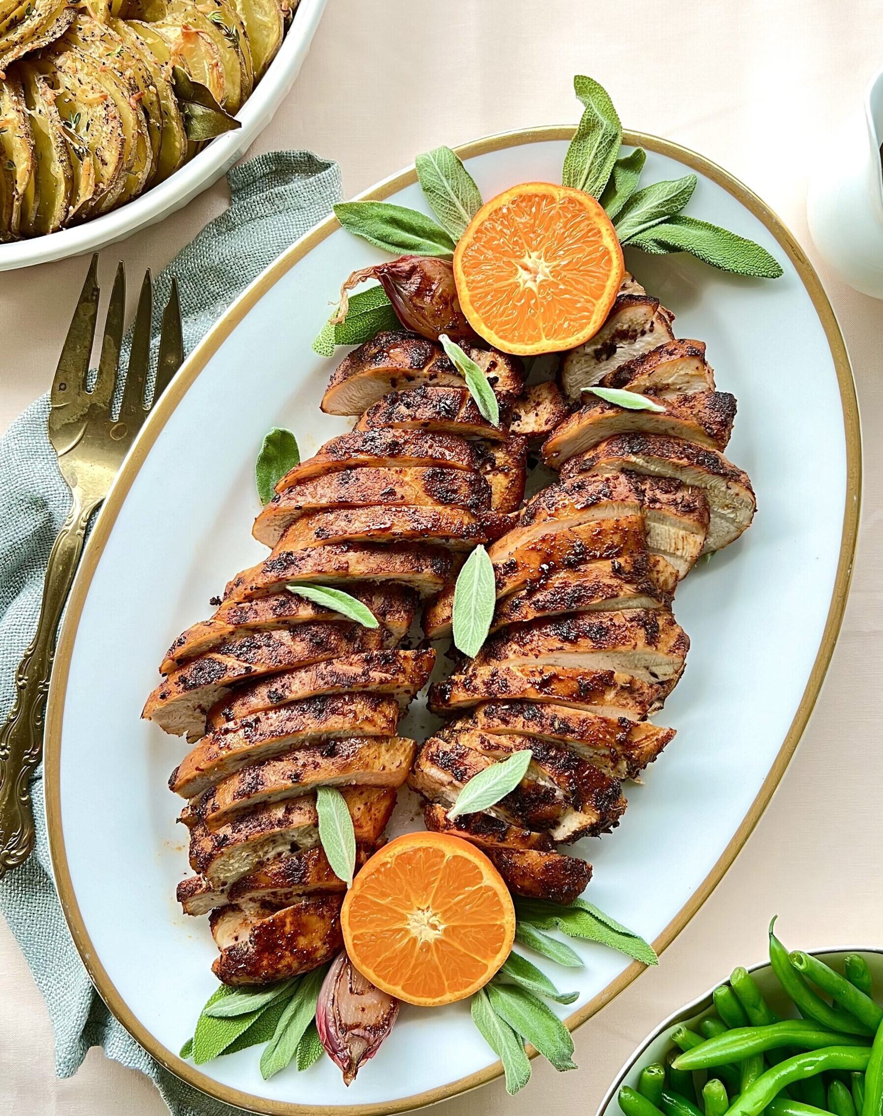 Overhead view of sliced turkey tenderloin on a platter. There is a cut orange on each end and a pitcher of gravy on the side.