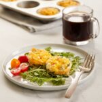 Egg muffins on a white plate. Side view. The muffins are resting on a bed of arugula and with tomatoes on the side.