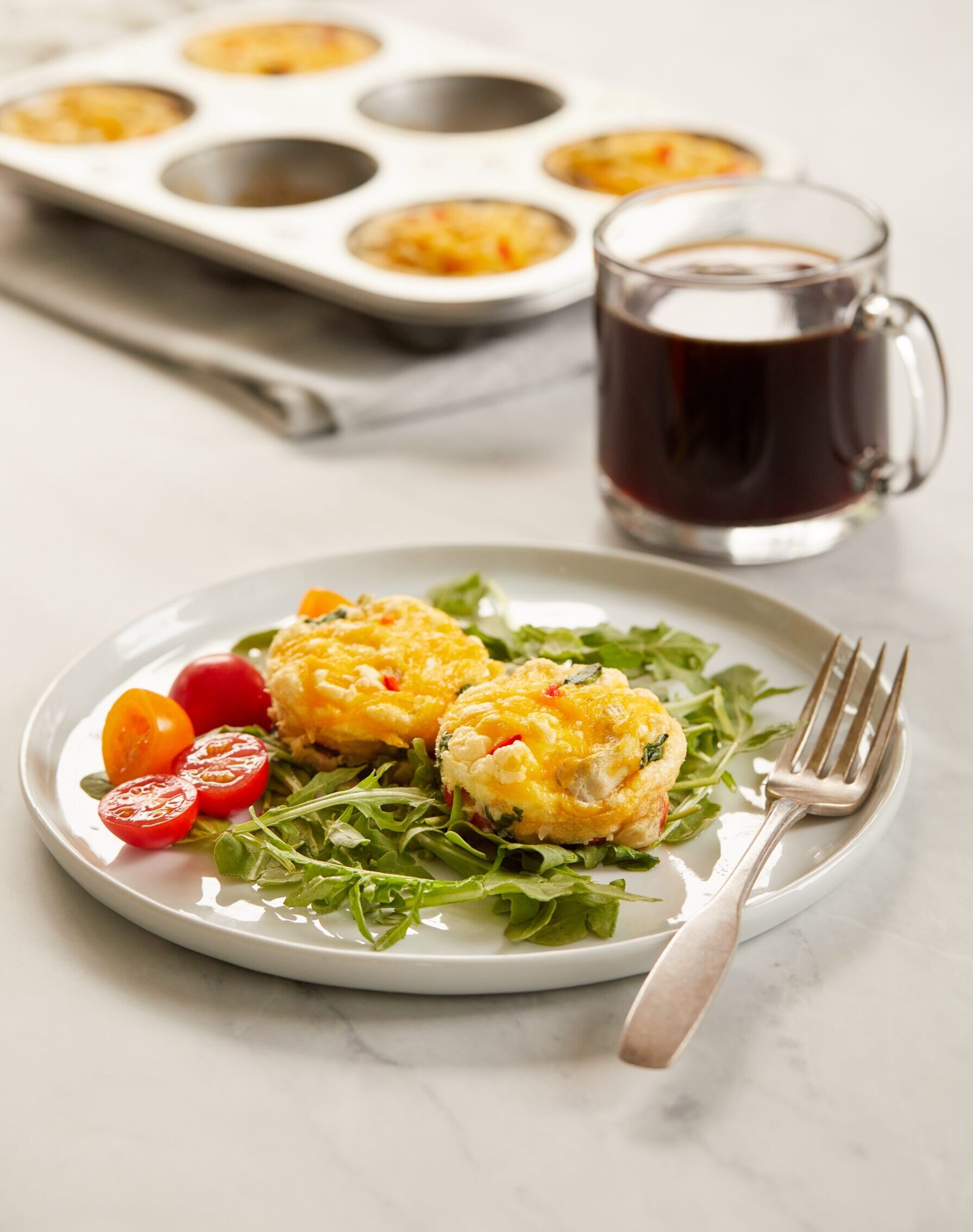 Egg muffins on a white plate. Side view. The muffins are resting on a bed of arugula and with tomatoes on the side.