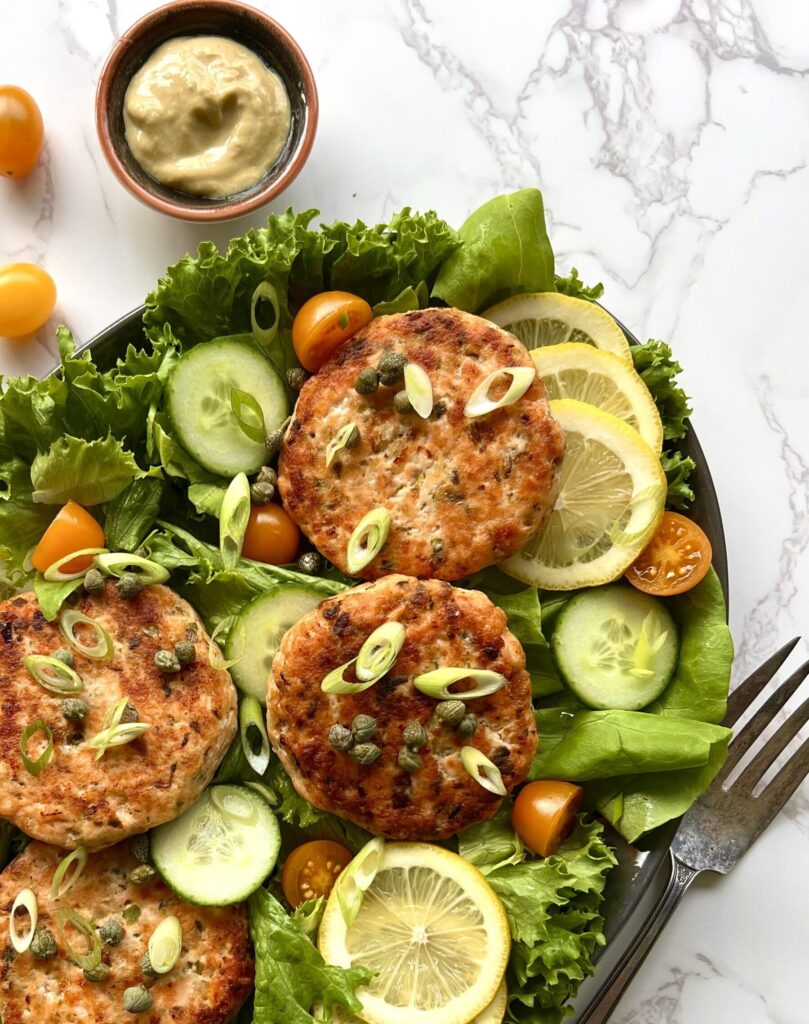 Platter of 4 salmon burgers over fresh vegetables and lemon slices. Overhead view.