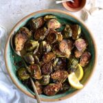 Overhead view of roasted brussel sprouts in a blue bowl with a brown rim. It is on a white marble background with a small bowl of paprika on the side.