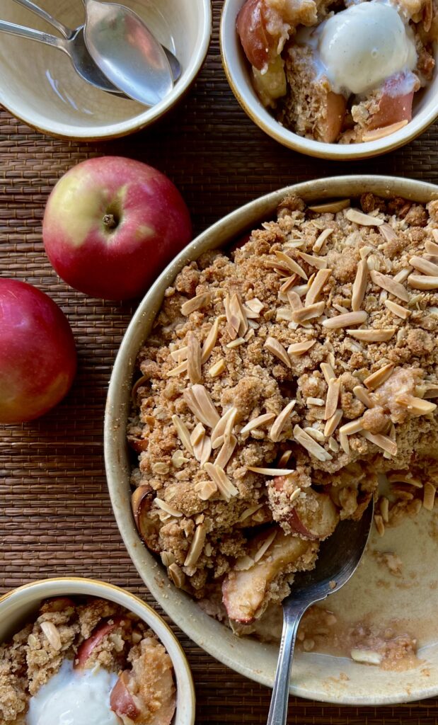 Overhead shot of 1/2 of the pie dish that has the apple crumble inside. On the side are 2 whole red apples for decoration.