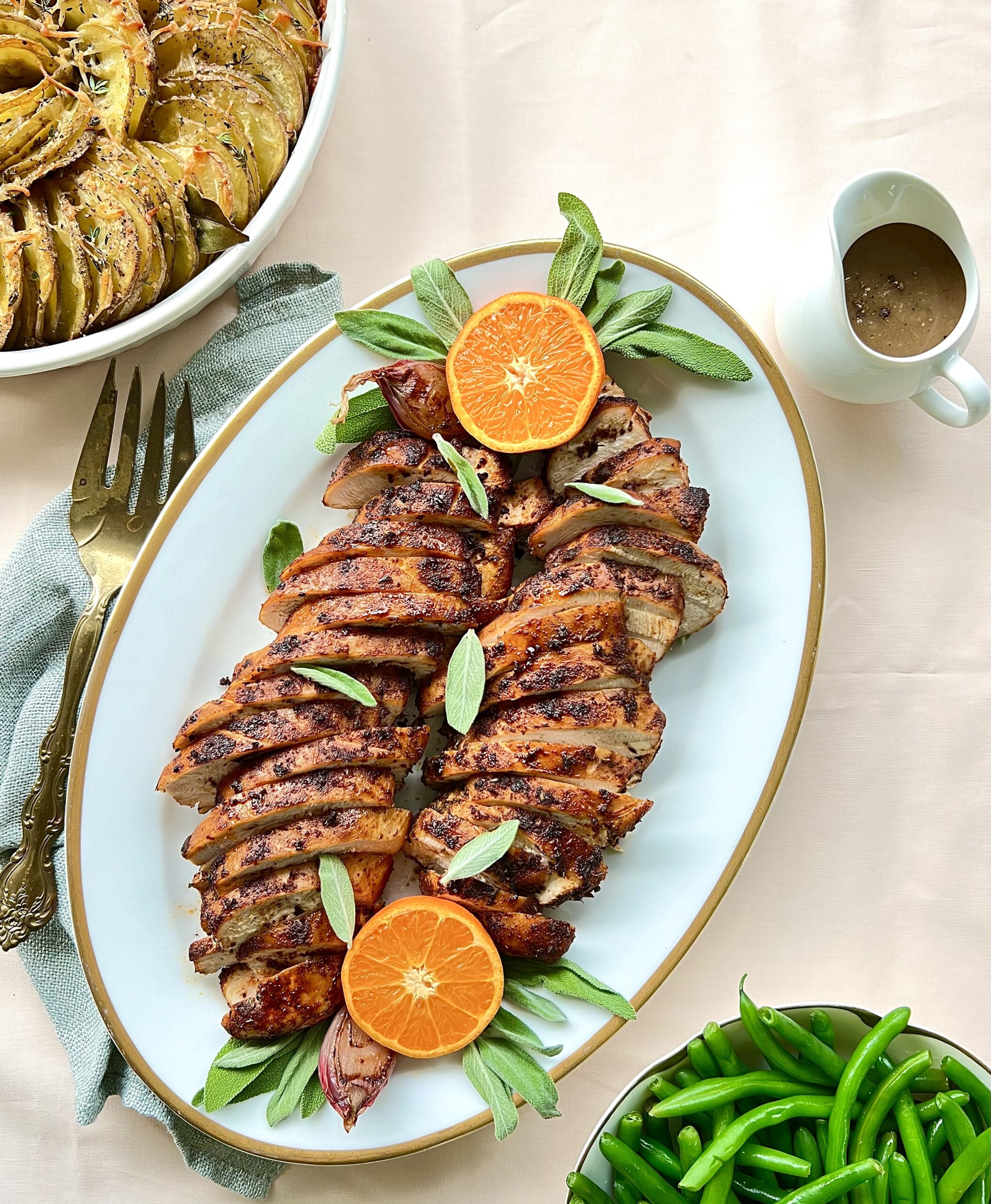 Overhead view of sliced turkey tenderloin on a platter. There is a cut orange on each end and a pitcher of gravy on the side.