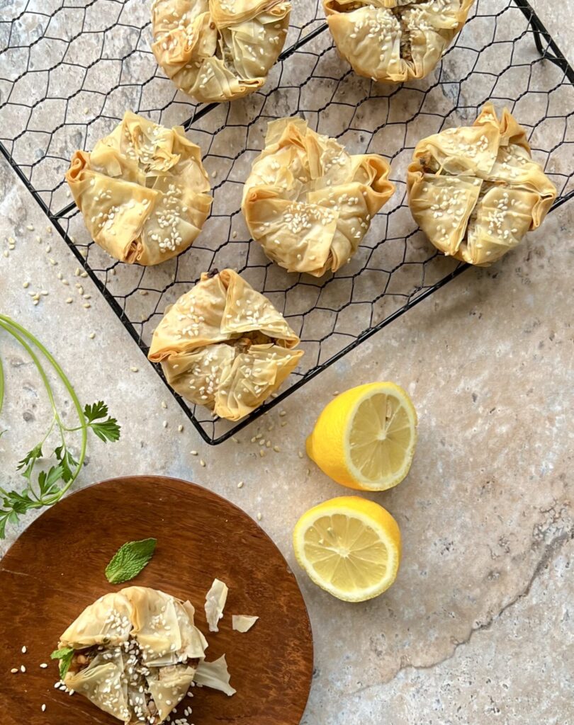 The tartlets are resting on a wire rack with a cut lemon framing it on the side and a plate on the lower left corner with one tartlet on it. The plate is rust colored.