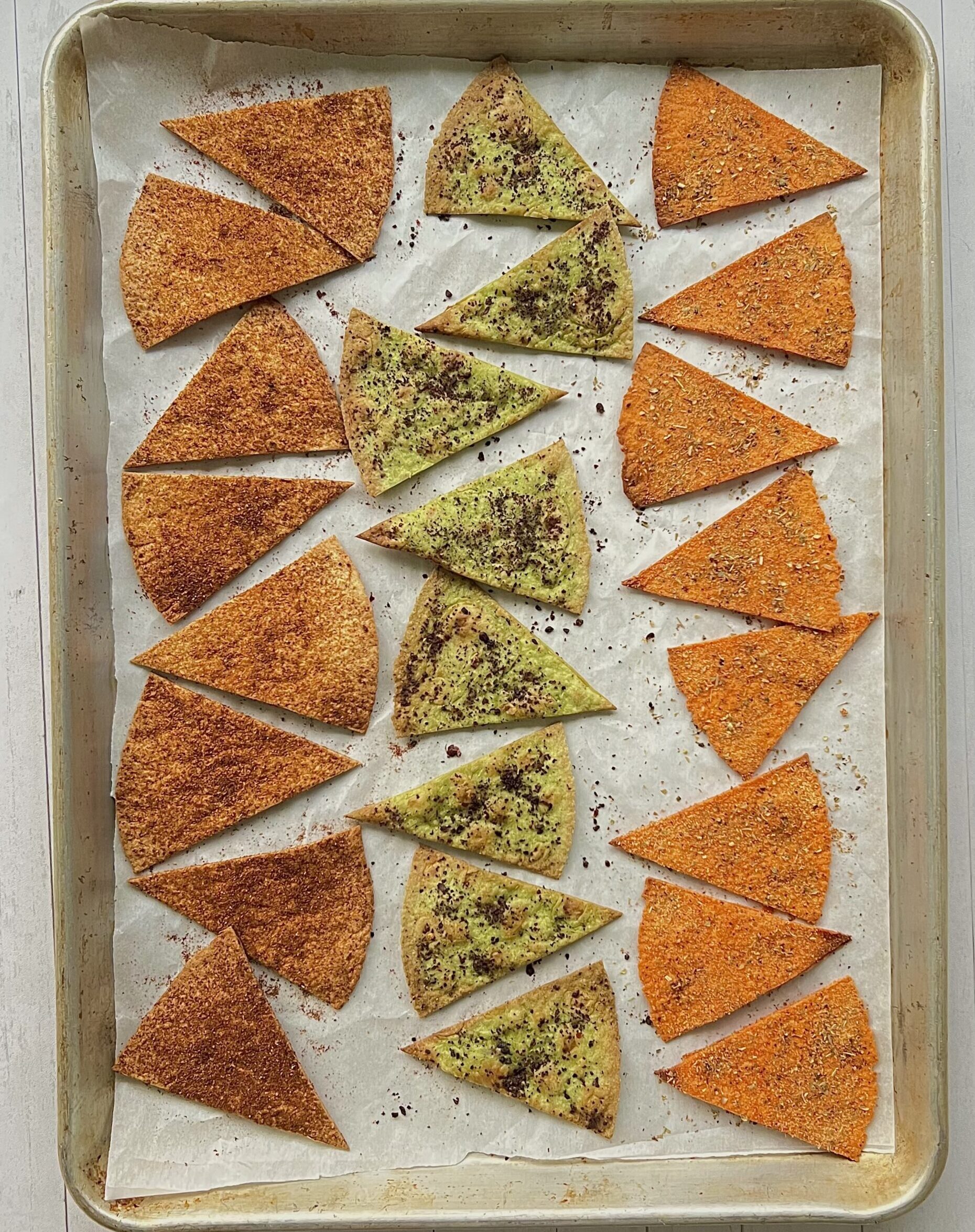 Baking dish with 3 rows of tortillla chips on it. The outer rows are orange and the inner row of chips are green tinged.