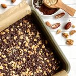 Overhead view of a pan of walnut topped brownies. The pain is off center, half of it is shown on the picture and it is on a white background with scattered dates.