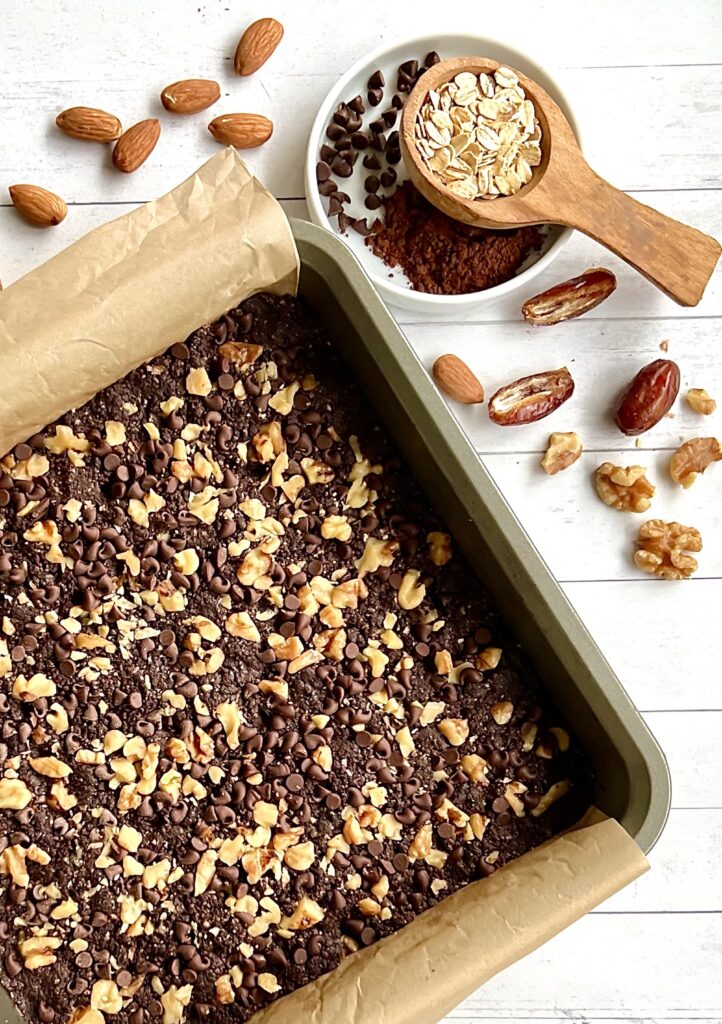 Overhead view of a pan of walnut topped brownies. The pain is off center, half of it is shown on the picture and it is on a white background with scattered dates.