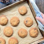 Overhead view of a baking sheet with half of it shown. It has cooked chocolate chip cookies on them and a hand holding the pan.