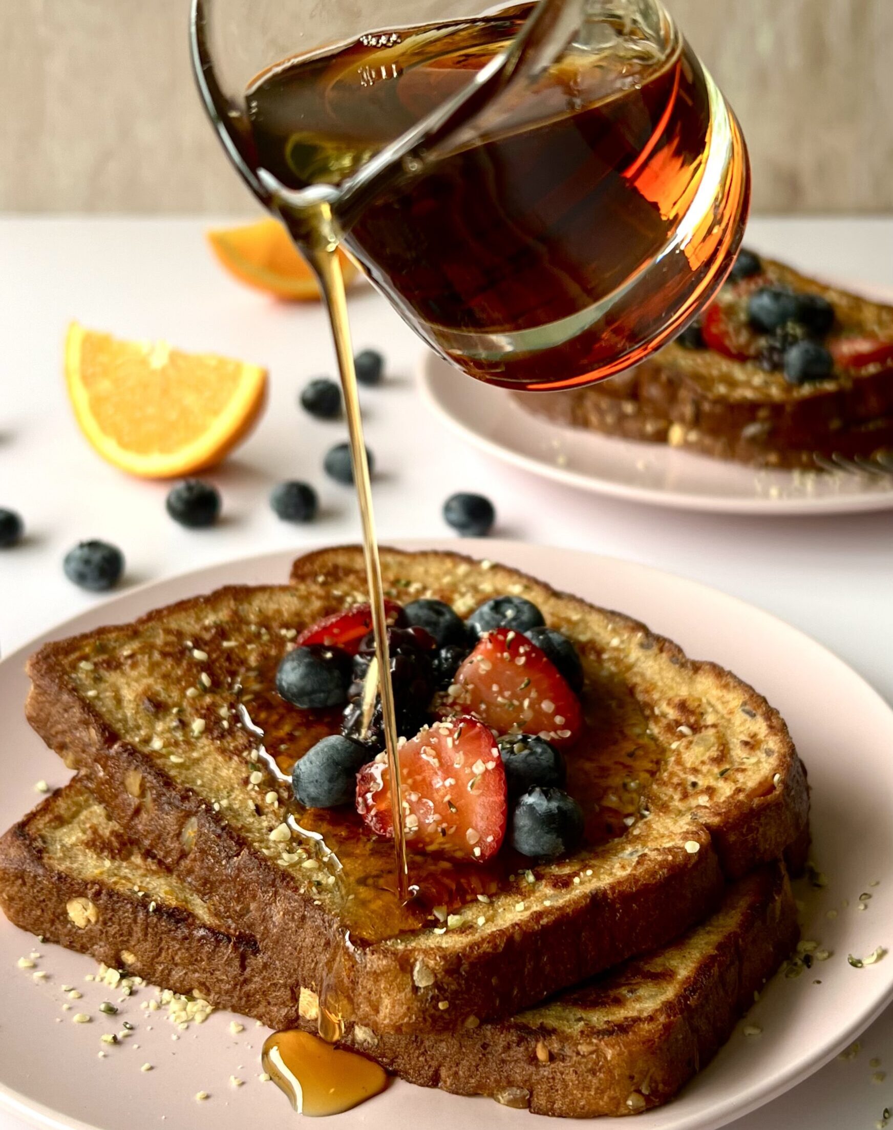 2 pieces of french toast with syrup being actively poured over top of them. There are berries on the french toast.