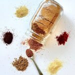 Glass jar of spice mix with individual spices piled up around the side.