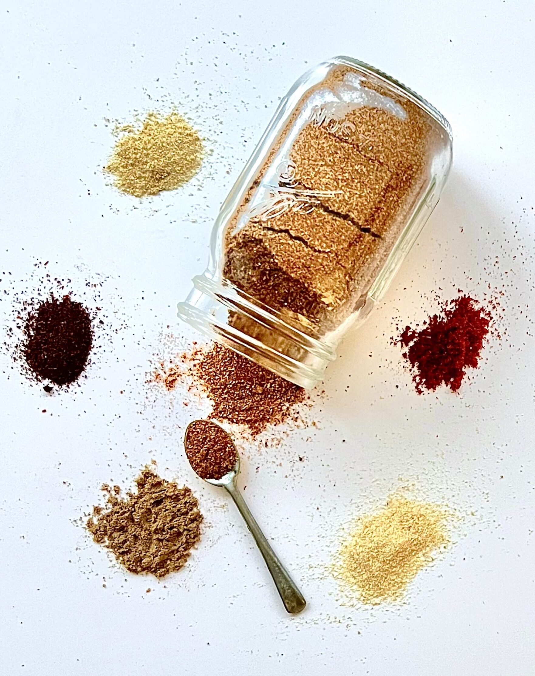 Glass jar of spice mix with individual spices piled up around the side.