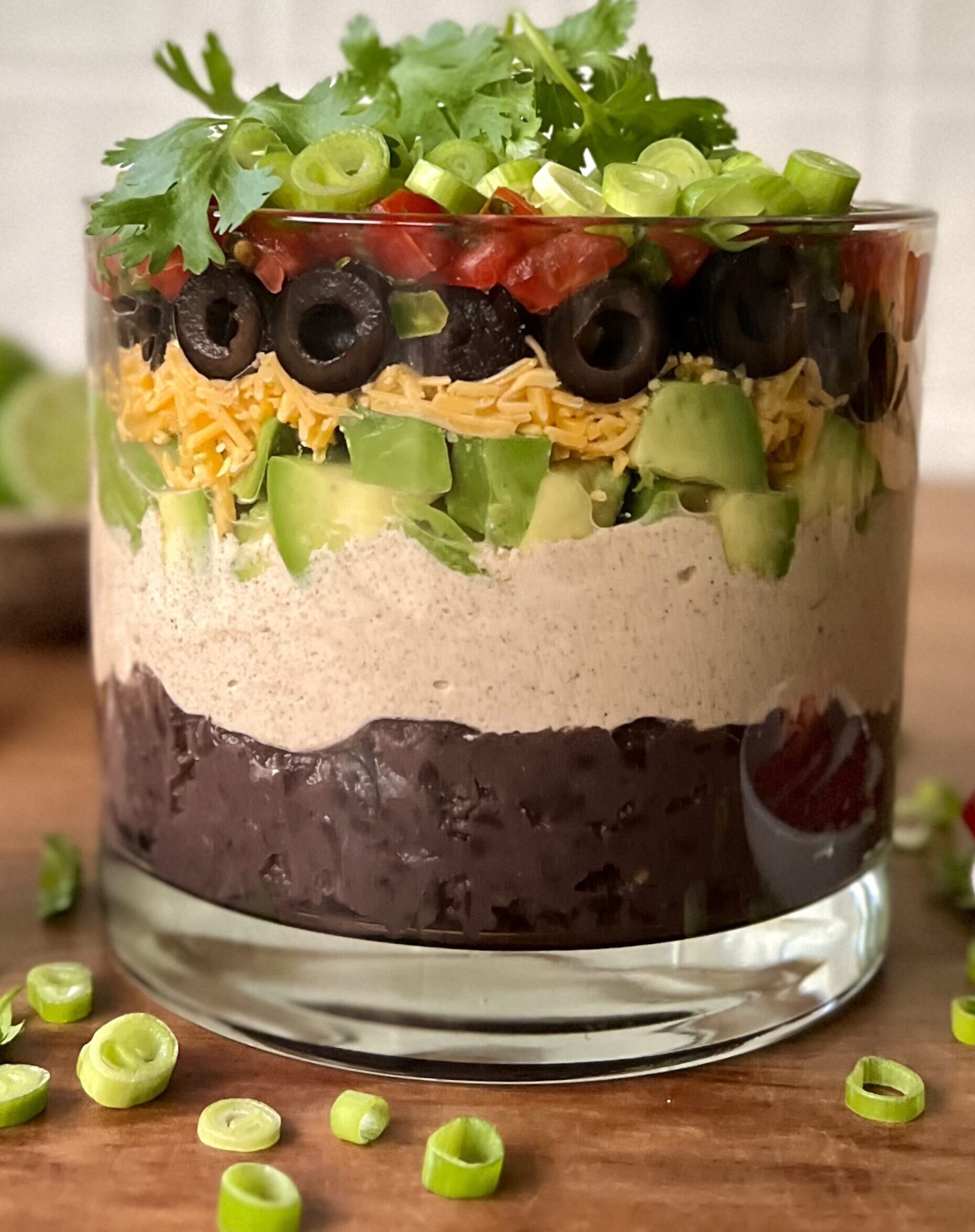 Sideways view of the bean dip in a glass jar. You can see each layer clearly. It is on a wooden cutting board.