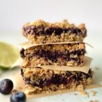 Side view of 3 blueberry oat bars stacked on top of one another with parchment paper in between.