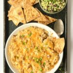 Overhead view of a bowl of the buffalo dip with homemade tortilla chips on the side and a small bowl of the cilantro lime relish.