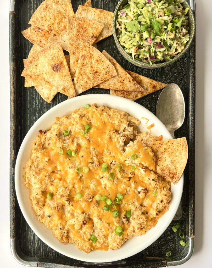 Overhead view of a bowl of the buffalo dip with homemade tortilla chips on the side and a small bowl of the cilantro lime relish.