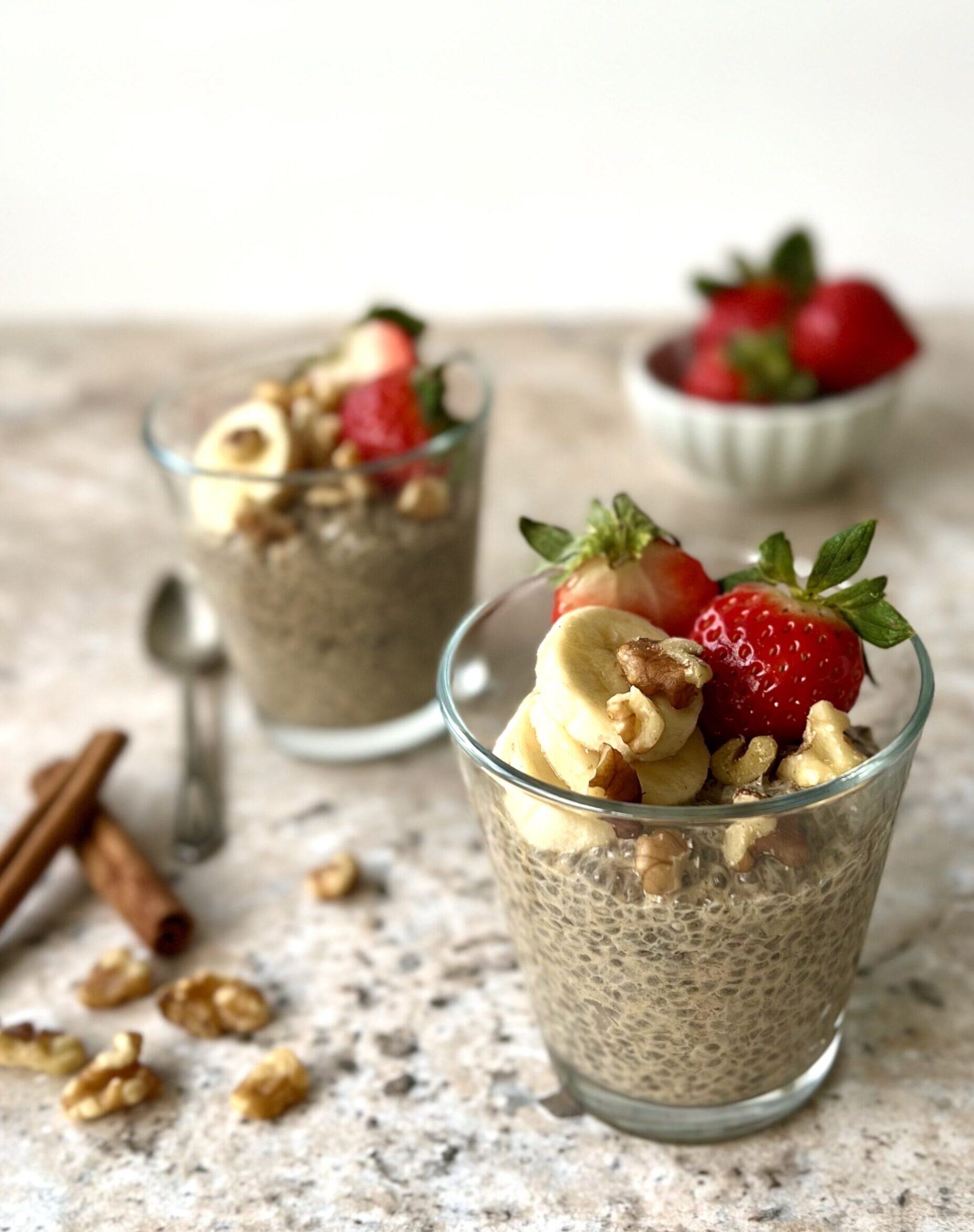 3/4 overhead view of 2 cups of the maple chia pudding topped with nuts, strawberries and banana