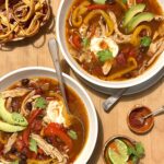 Overhead view of two bowls of bean soup on a wooden cutting board background and a piece of parsley and a cup of jalepenos in the background.