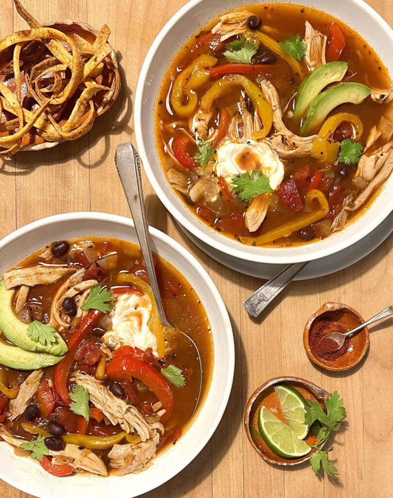 Overhead view of two bowls of bean soup on a wooden cutting board background and a piece of parsley and a cup of jalepenos in the background.