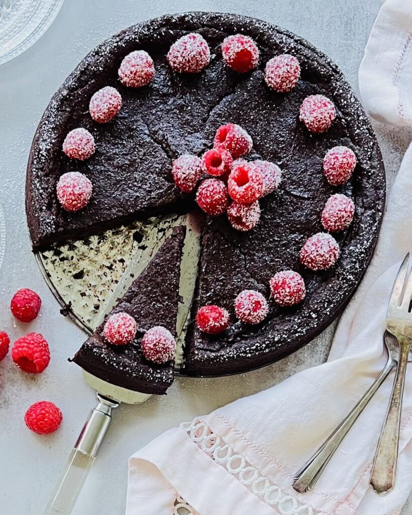 Overhead view of a chocolate cake with raspberries around the edge and a sprinkle of powdered sugar.