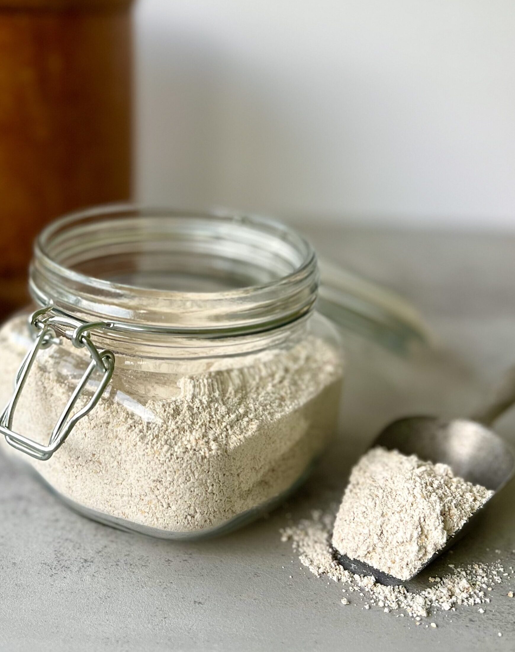 3/4 overhead view of a glass jar of oat flour and to the side if a silver spoon with a spoonful of the flour.