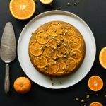 Overhead view of the cake with all the orange slices neatly arranged on top . The cake is on a white place with a blue background.