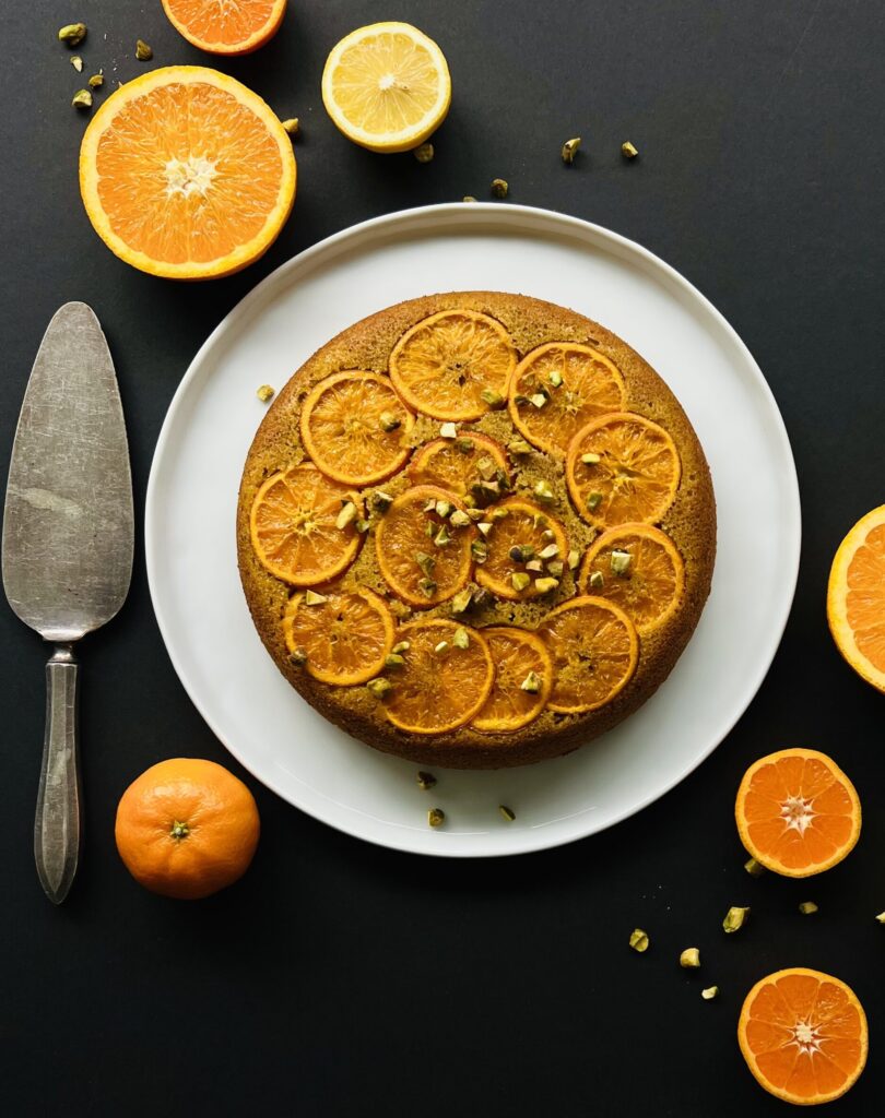 Overhead view of the cake with all the orange slices neatly arranged on top . The cake is on a white place with a blue background.