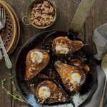 Overhead view of 4 roasted pears in an iron pot on a wood table. The pears have Greek honey and granola on them.