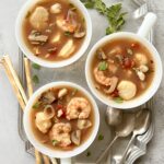 Overhead view of 3 white cups filled with seafood stew.