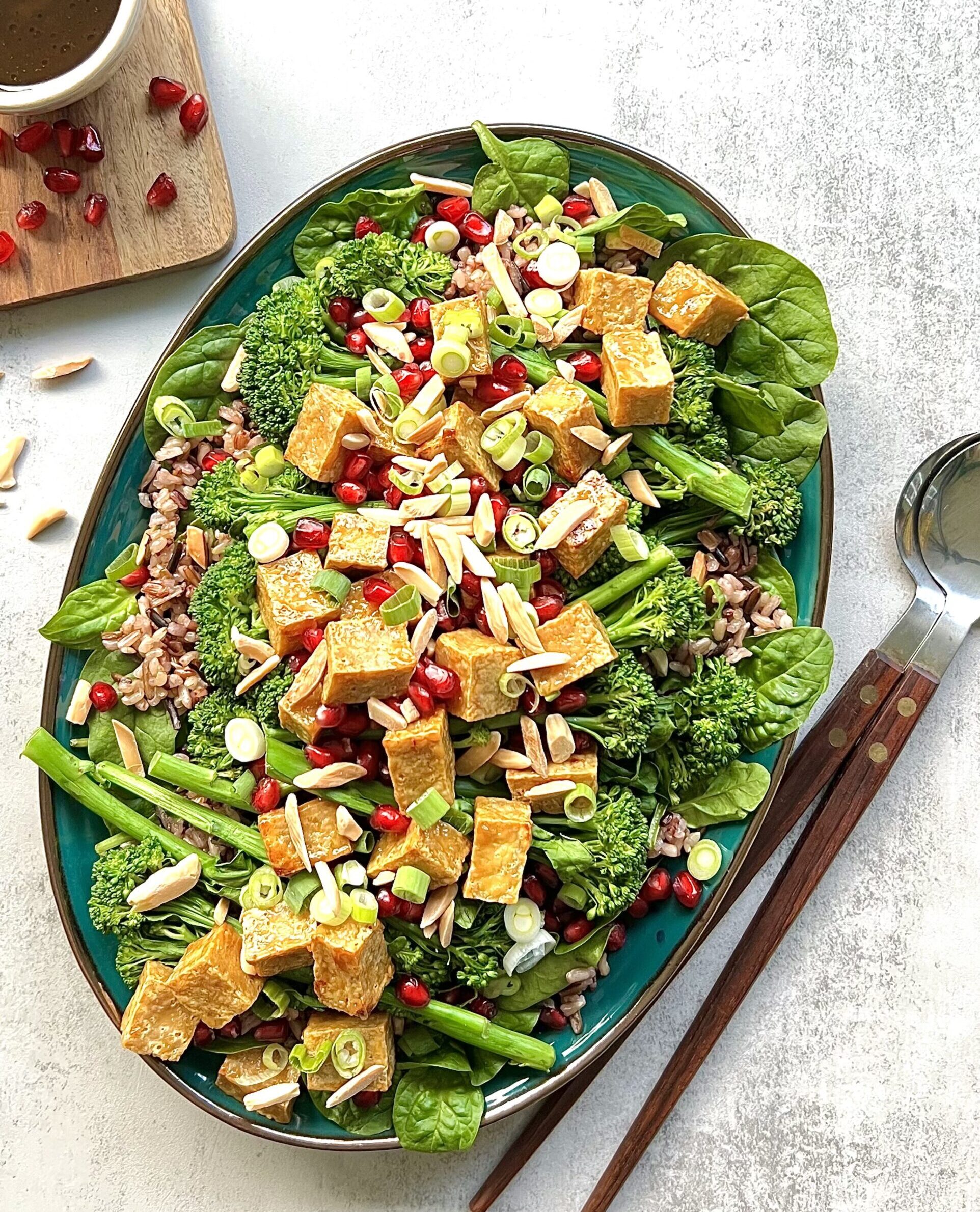 Overhead view of crispy tofu with pomegranate seeds and slivered almonds over top a bed of baby spinach and brown rice.