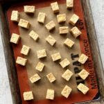 Overhead view of a baking sheet with cubes of baked tofu.